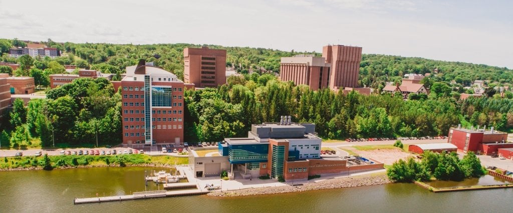 Aerial view of Michigan Technological University Campus with trees and brick skyscrapers in the background and a dock with boats 