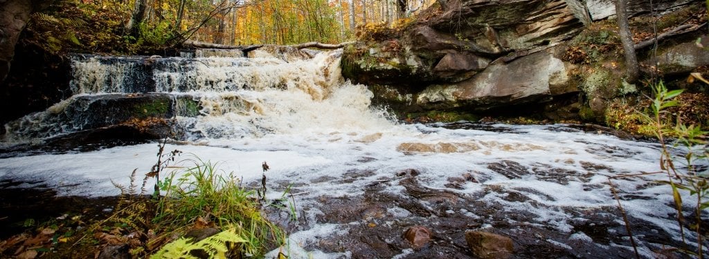 A waterfall flows over layers of brown and gray rock