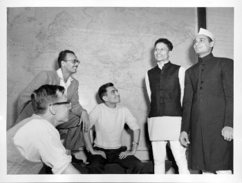 four men in traditional international garb stand in front of a world map in a black and white photo