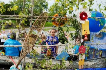 A young girl stands and two women elders of Keweenaw Bay Indian Community sit on the tribe's float entry as is it pulled down a street outside downtown