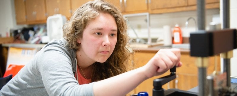 A young student turns the handle on a calibrating test machine to demonstrate in a lab