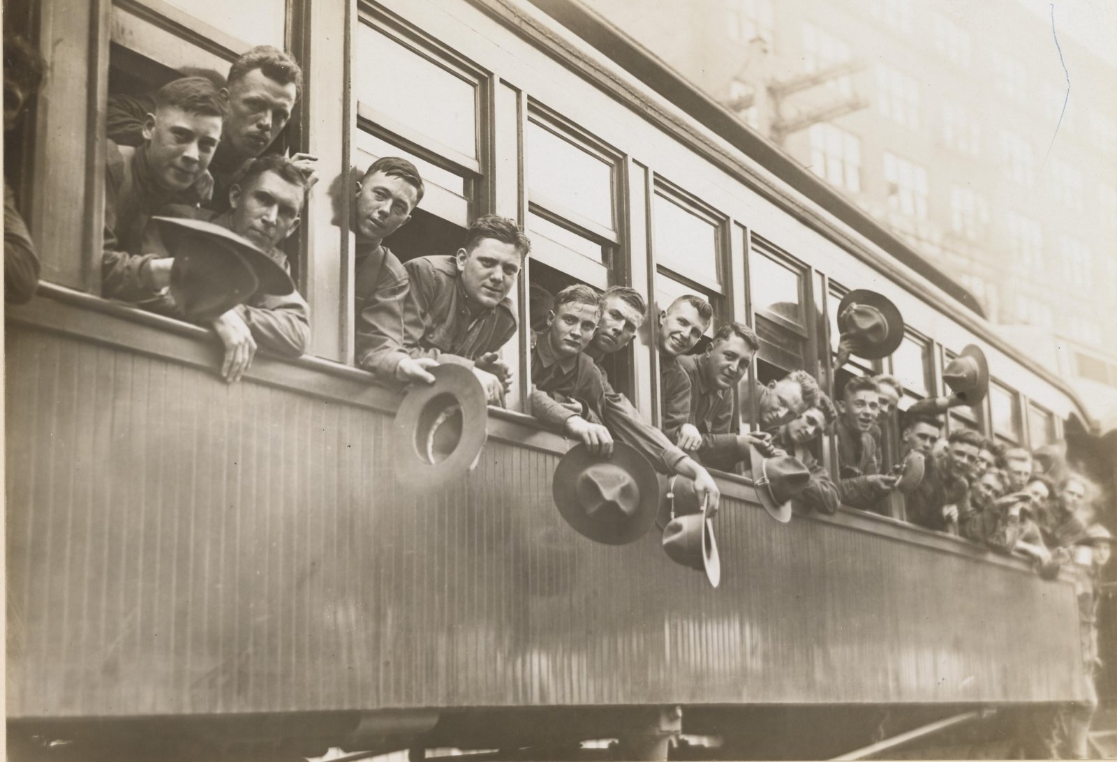 World War I soldiers black and white photo with their heads out the windows of a train in Cincinatti, Ohio waving to the unseen crowd at the train station