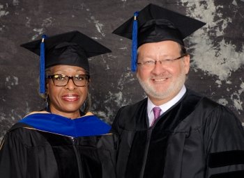 A woman and a man standing side-by-side in commencement ceremony regalia.