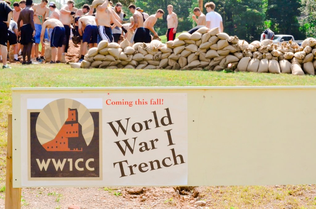 young men in a line fill burlap sacks with sand on a grassy hill with a sign in the forefront that reads World War I & the Copper Country ww1cc.mtu.edu