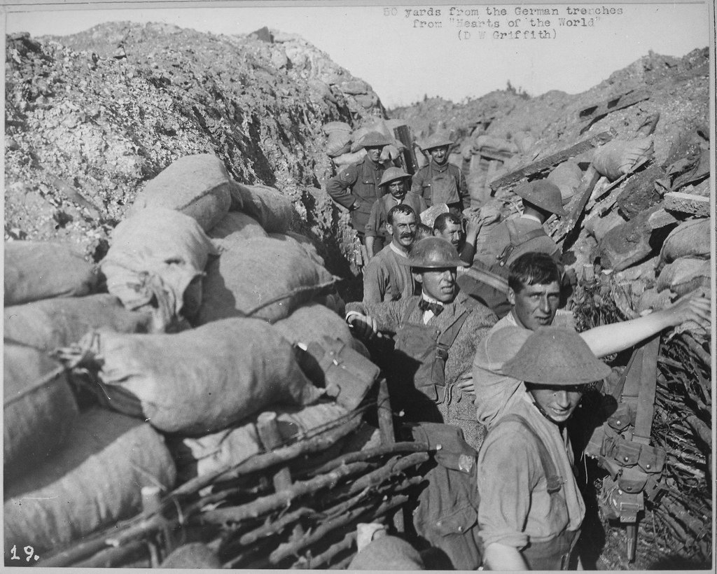 soldiers and filmmaker DW griffith in an earthen and sandbagged trench new the german lines after a bombing in a black and white World War I photo from the national archives the men are wearing metal helmets