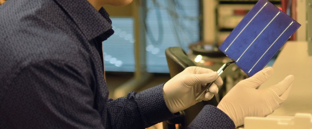 man wearing lab gloves holds a dinner plate-sized solar panel