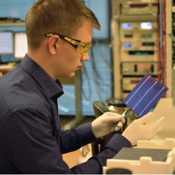 young man with safety glasses and gloves holds a small solar panel