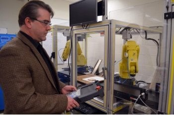 A man stands next to a yellow robotic arm in a lab