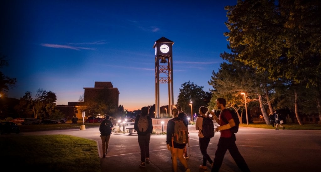 Students walk by the campus clock tower at dusk.