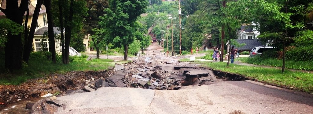 a steep road ripped up by water resulting in a street-wide sized hole