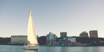 sailboat in the foreground on waters of the Portage Canal with campus buildings of the Great Lakes Research Center in the background 