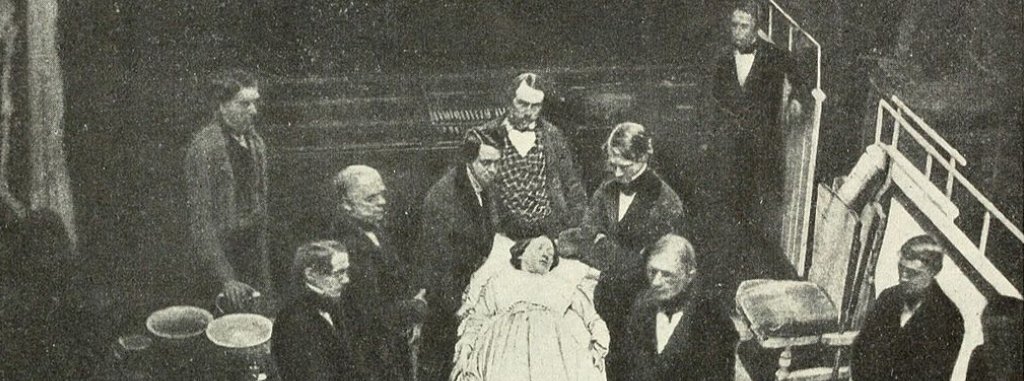 A historical photo of a group of men at Harvard clustered around a female patient on an operating table.