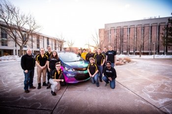 group of students around a brightly colored car
