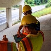 people in vests and hard hats standing under a bridge