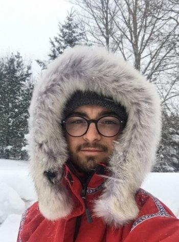 A young man wearing glasses and a heavy parka outside in the snow