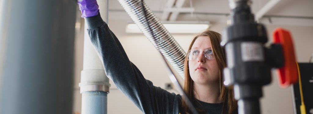 woman with gloves and safety glasses adjusts a valve