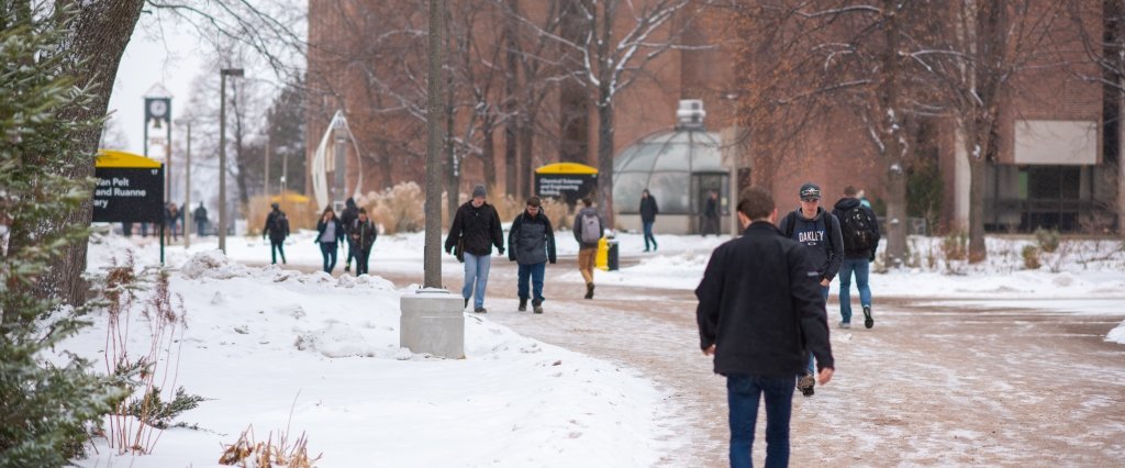 Students walking across campus while snow is falling.