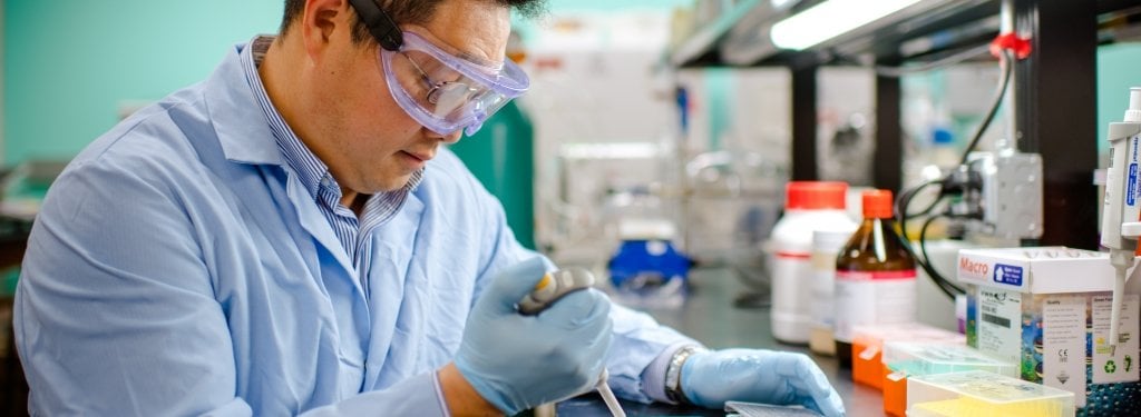 man in lab coat with glasses and gloves holding a syringe