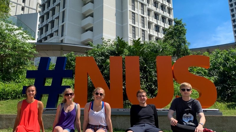 students sit in front of a campus sign