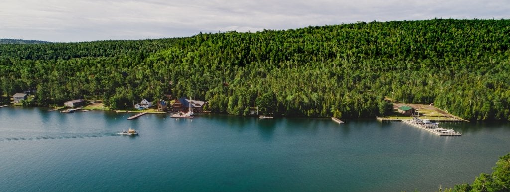 A gold and black boat in a harbor goes past shore homes and green forest in a Copper Harbor cove