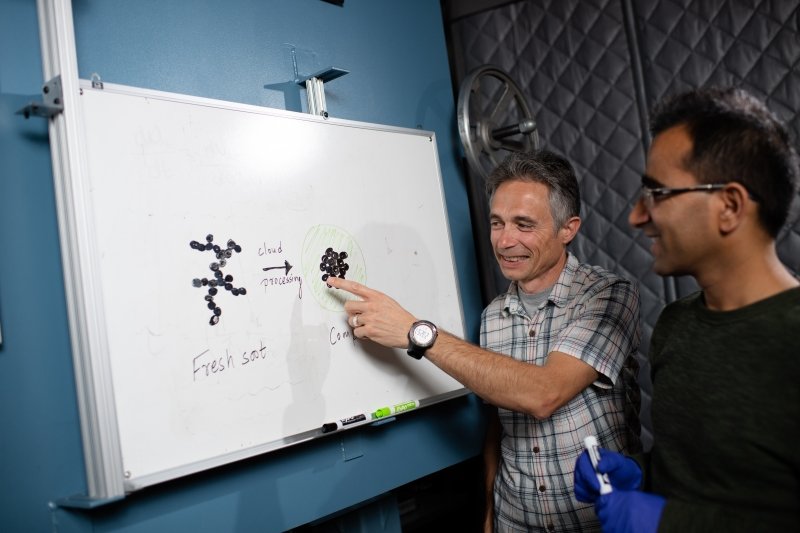 Two men look at a whiteboard where a diagram of how soot compacts is drawn.