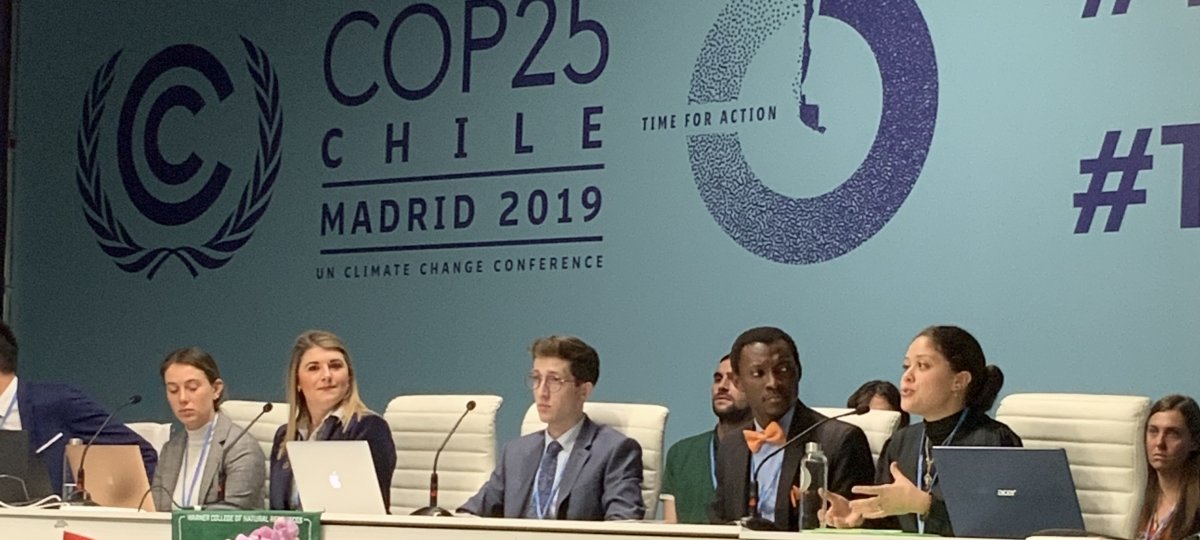 Five students sitting at a table presenting research findings. The banner behind them reads "COP25 Chile Madrid 2019 UN Climate Change Conference."