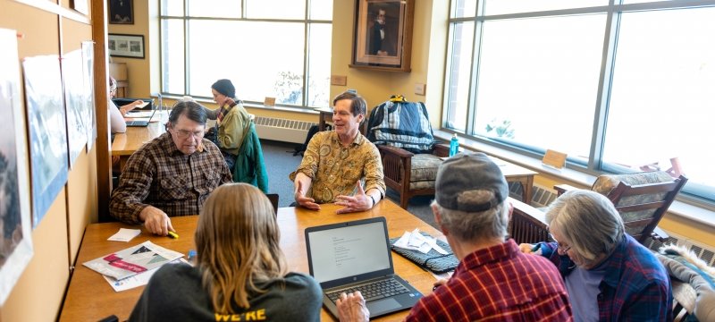 A group of people in a library with windows to one side.