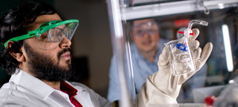 two men in lab coats and eyewear looking at a beaker