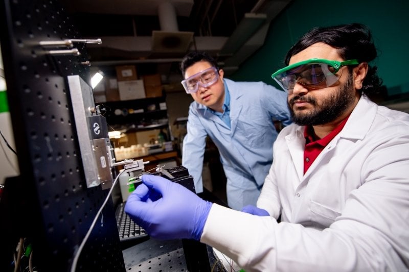 two men in lab coats holding metal equipment