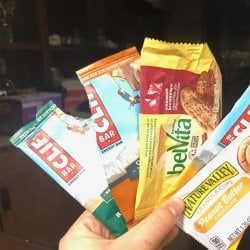 Three Clif, a Belvita and one Nature Valley granola cups wrappers held closeup in a hand with a brown background