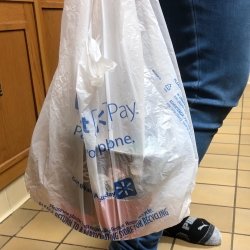 Walmart shopping bag with person's legs in jeans wearing Puma socks on a tile kitchen floor with kitchen cabinets in the background