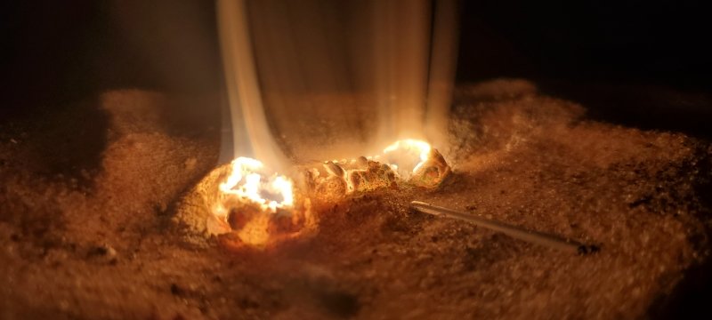 Two flame holes and a piece of metal from a student design project with orange glowing coals.