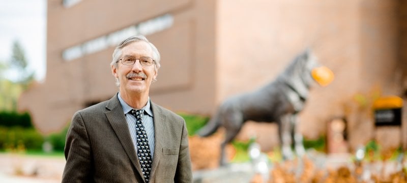 man with mustache smiling in front of husky statue on Michigan Tech campus