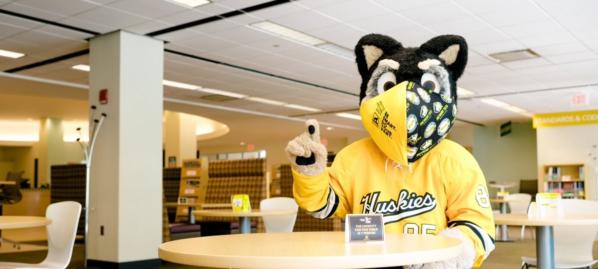 The pandemic has changed the way we teach and learn. Physical distancing, masks and Zoom classes are part of our current reality. masked mascot Blizzard sits in the library