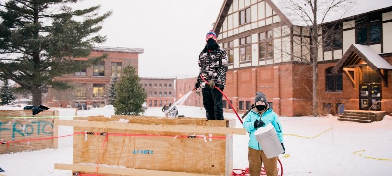 Two students wearing masks work on snow statue