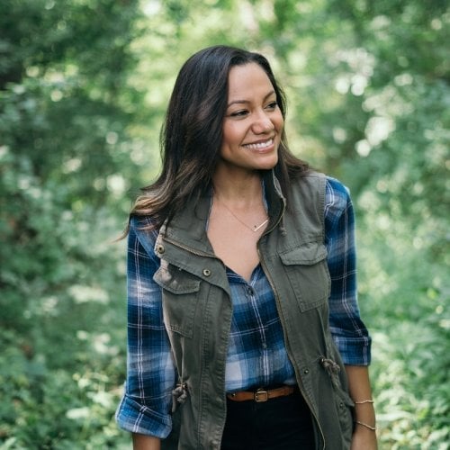 A woman smiles at something in the distance in a green forest.