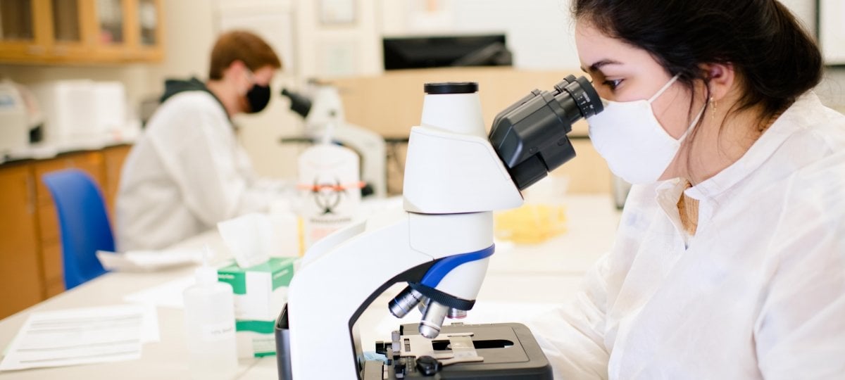 The Michigan Tech's COVID-19 testing lab’s anniversary is April 22 and Medical Laboratory Professionals Week is April 18-24. Two people look through microscopes in a lab.