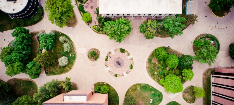 Drone image of Husky statue; top down perspective of green trees, gardens, sidewalks, and buildings.