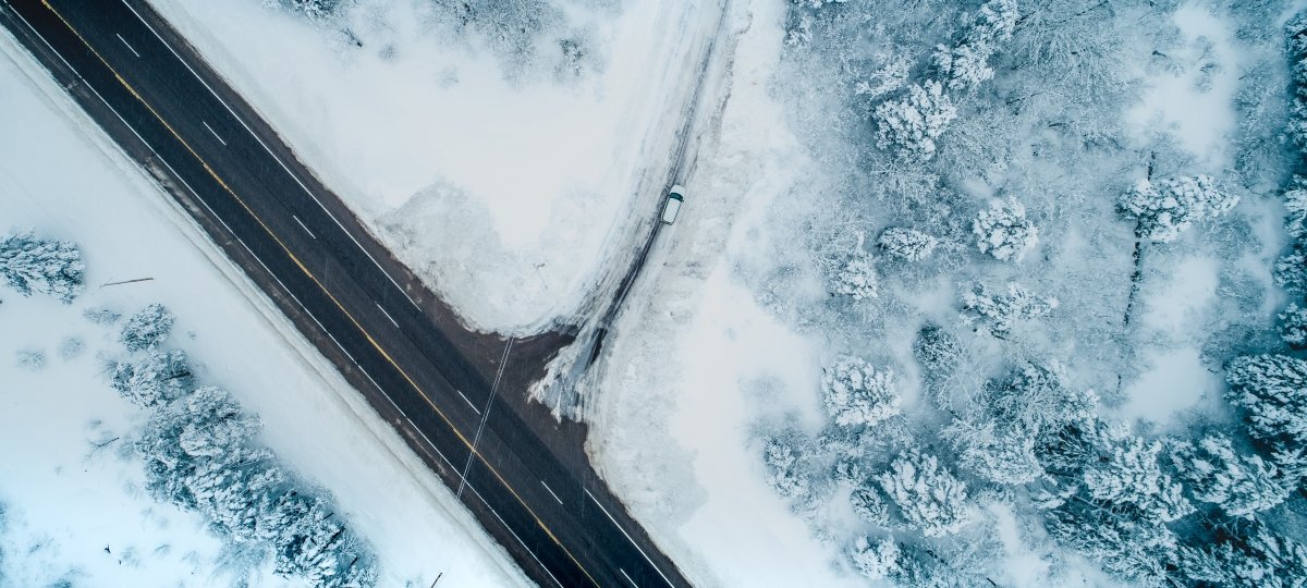 From an overhead drone perspective, a car drives on a snowy road. 