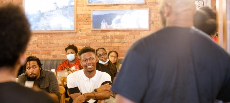 Six people facing us with a brick wall background in a Greektown pizzeria at the African American Alumni Association gathering for Michigan Tech in Detroit. Two people have their backs to the camera.