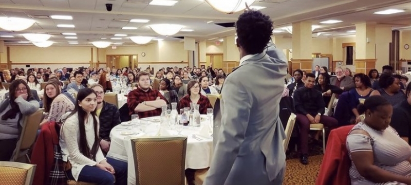 The back of a man in a suit addressing a crowd in a ballroom at Michigan Tech.
