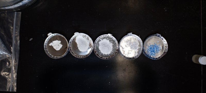 Varying sizes of plastic fragments in five different petri dishes on a countertop.