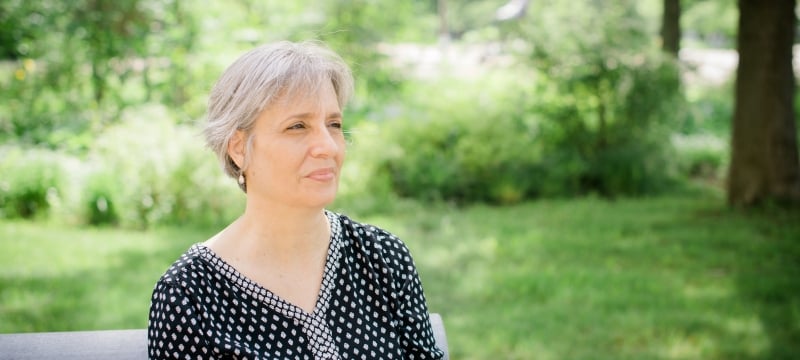 A woman smiles with a green space and park bench behind her on the Michigan Tech campus.