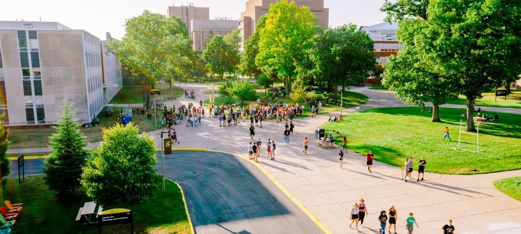 An aerial of students on campus with green trees, brick buildings, and sidewalks at Michigan Tech.