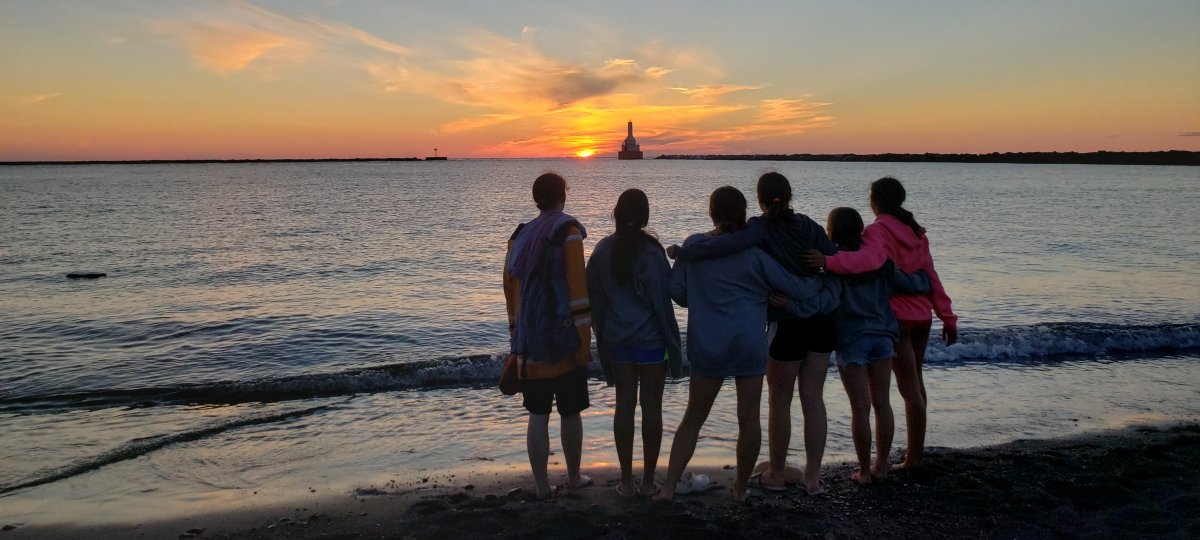 Six SYP participants watch the sunset behind a lighthouse on Lake Superior.