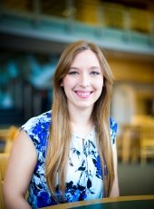 A young woman with a blue stairway background smiles at the camera at Michigan Tech in 2018.