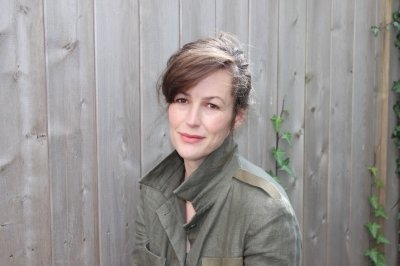 A woman smiles with a wooden plank fence and two trailing green vines behind her in a portrait.