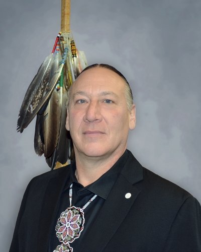 A man in a portrait with Native American feathers in the background.