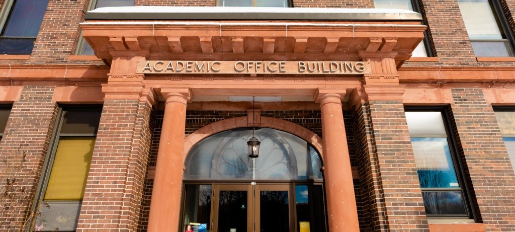 The brick facade of MTU's College of Business with lettering that says Academic Office Building and glass entry doors.