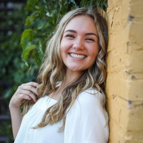 A young woman leans against a tree smiling with a green background in her senior picture. She is Michigan Tech's 2022 Impact Scholar.